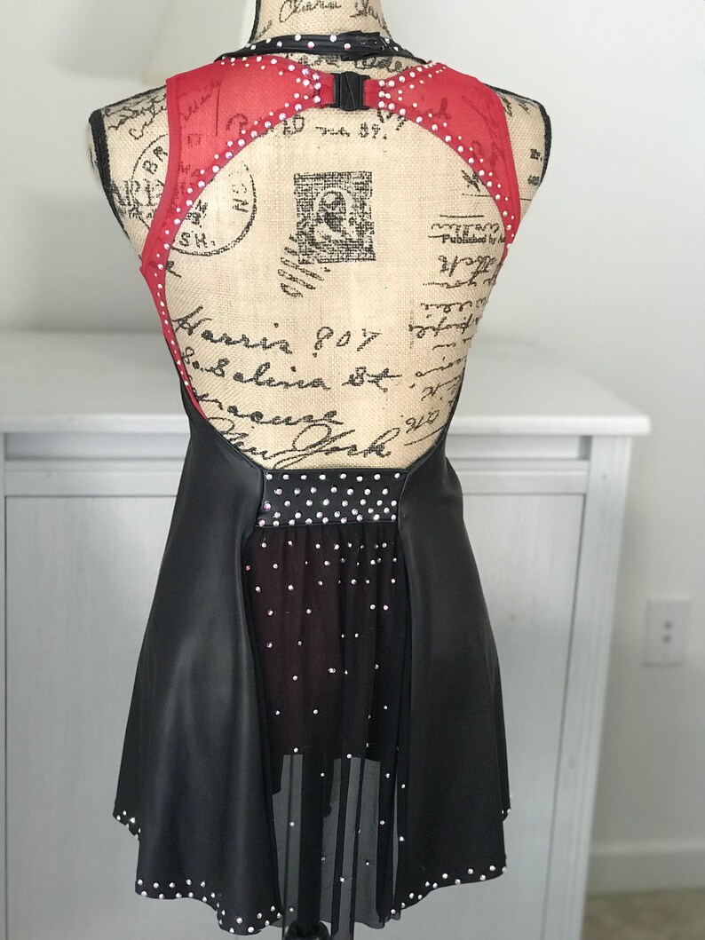 May include: Black and red figure skating dress with a mesh skirt and rhinestones. The dress has a low back and a scoop neckline.
