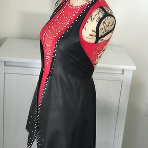 May include: A black faux leather vest with a red mesh top underneath. The vest has a scoop neck and a flared hem. Both the vest and top are embellished with rhinestones.