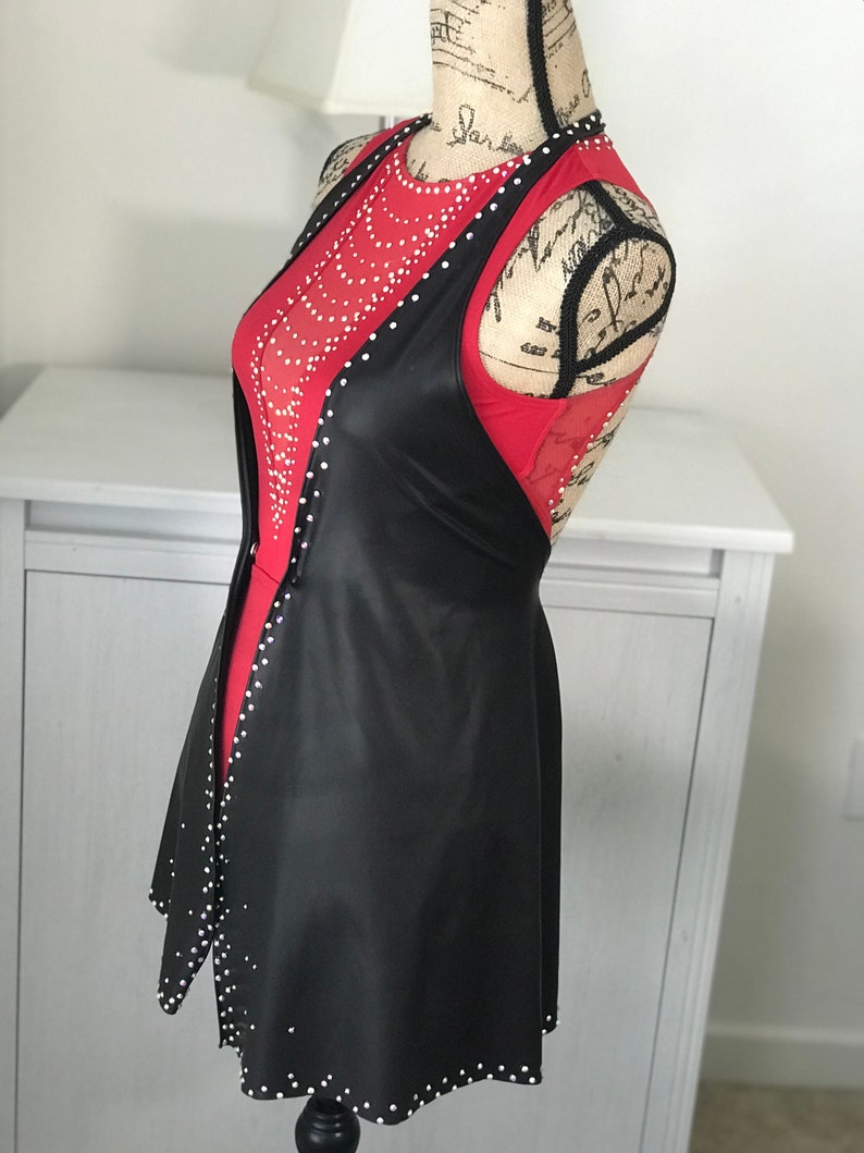 May include: A black faux leather vest with a red mesh top underneath. The vest has a scoop neck and a flared hem. Both the vest and top are embellished with rhinestones.