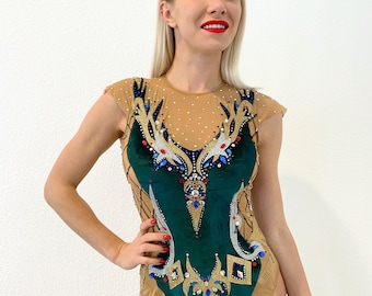 May include: A green and gold leotard with a mesh overlay and rhinestones. The leotard has a unique design with a geometric pattern and a pointed neckline.
