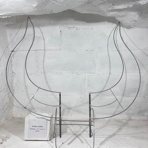 May include: A metal wire frame sculpture of a bull's head, with two large horns and a detailed face. The sculpture is mounted on a white wall and is partially obscured by a white ceiling. A small white box with the text "Atelier Louise" is in the foreground.