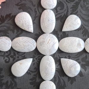 Könnte beinhalten: Eine Sammlung von 13 weißen Achat-Tropfencabochons, die in einem Sternmuster auf einem schwarzen Hintergrund angeordnet sind.