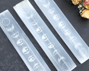 May include: Three white selenite sticks with etched moon phases. The sticks are approximately 6 inches long and are arranged in a triangular shape.