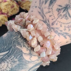 May include: A bracelet made of pink and white gemstone chips. The bracelet is made of multiple strands of chips and is worn on a person's wrist.
