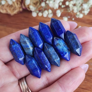 May include: A collection of eight blue lapis lazuli crystal points, each with a unique shape and size. The points are arranged in a fan shape, with the largest point at the top and the smallest point at the bottom.
