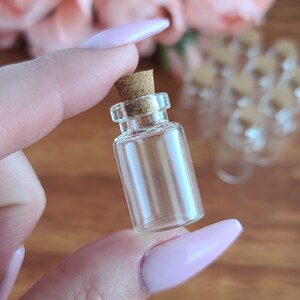 May include: A small, clear glass bottle with a cork stopper. The bottle is about 2 inches tall and is perfect for holding small items like essential oils, herbs, or spices.