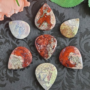 May include: Seven agate gemstone cabochons in various shades of red, white, and green. The cabochons are shaped like teardrops and have a polished finish.