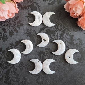 Könnte beinhalten: Acht weiße Achat-Mondsteine in Halbmondform auf schwarzem Hintergrund. Die Steine sind poliert und haben ein natürliches, organisches Aussehen.