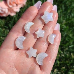 May include: A collection of seven moon and star shaped rainbow moonstone crystals. The crystals are white with iridescent rainbow colors.