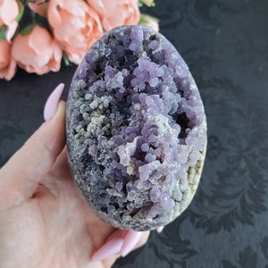 Könnte beinhalten: Eine violette Achat-Geode mit einem Cluster aus kleinen, violetten Kristallen. Die Geode ist glatt und poliert, und die Kristalle funkeln.