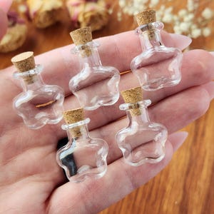May include: Five small glass bottles with cork stoppers shaped like stars. The bottles are clear and empty.