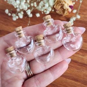 May include: Five small glass heart-shaped bottles with cork stoppers. The bottles are clear and empty.