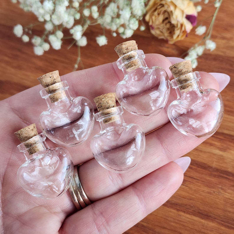 May include: Five small glass heart-shaped bottles with cork stoppers. The bottles are clear and empty.