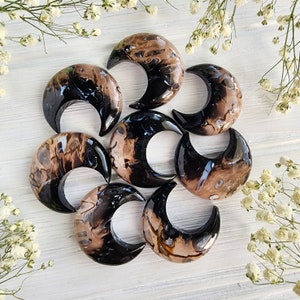 Könnte beinhalten: Sieben polierte Achat-Steine in Halbmondform mit schwarzer und brauner Marmorierung. Die Steine sind in einem Kreis auf einer weißen Holzoberfläche angeordnet.