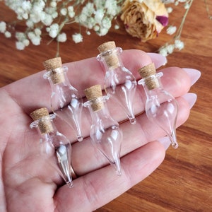 May include: Six small, clear glass bottles with cork stoppers. The bottles are teardrop shaped and have a pointed tip.