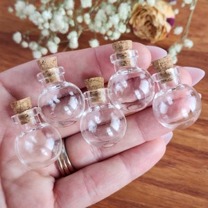 May include: Five small, clear glass bottles with cork stoppers. The bottles are round and have a smooth, shiny finish. They are perfect for holding small items, such as essential oils, herbs, or spices.