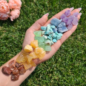 Könnte beinhalten: Eine Hand hält einen Regenbogen aus kleinen, abgerundeten Steinen, darunter Amethyst, Türkis, grüner Aventurin, Citrin und Karneol.