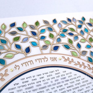 May include: A white background with a decorative wooden tree design. The tree has branches with leaves in shades of blue, green, and gray. The text "אני לדודי ודודי לי" is written in Hebrew on a brown banner at the bottom of the image.