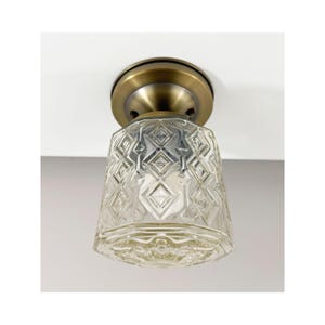 May include: A vintage ceiling light fixture with a clear, diamond-patterned glass shade. The shade hangs from a brass-colored metal base. The light fixture is mounted on a white ceiling.