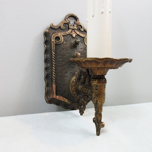 May include: A vintage brass wall sconce with an ornate design. The sconce has a single candle holder and a decorative backplate.