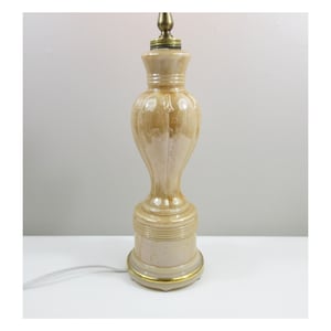 May include: A ceramic table lamp with a cream-coloured base and gold accents. The base is shaped like a vase with a fluted design.