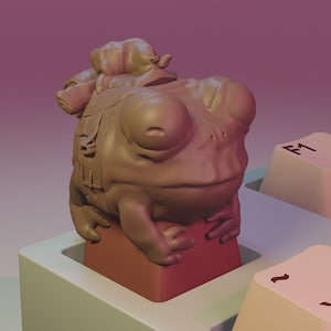May include: A quirky, brown frog ornament sitting on a keyboard key. The keyboard features off-white keys with black symbols and numbers. The background has a gradient of pink and purple.