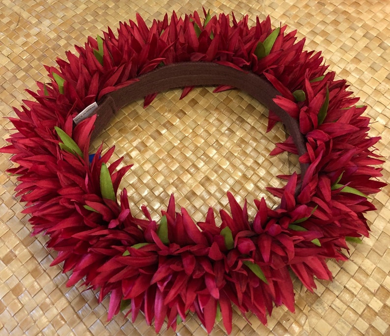 Puede incluir: Un lei floral rojo vibrante con acentos verdes y una banda marr&oacute;n. El lei est&aacute; hecho de numerosos p&eacute;talos rojos y hojas verdes, dispuestos en un patr&oacute;n circular. El lei es una guirnalda hawaiana tradicional.