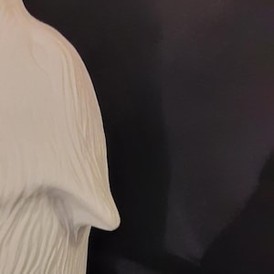 May include: White ceramic wolf figurine with a detailed fur texture. The wolf is sitting with its head tilted back and mouth open, as if howling.