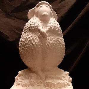 May include: White ceramic sculpture of a sheep with a fluffy coat. The sheep is standing on a base with a decorative design. The base has the text "Ewe's not fat, Ewe's just fluffy" inscribed on it.