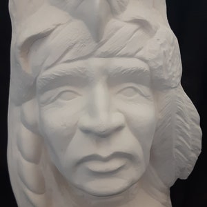 May include: White plaster sculpture of a Native American man's head with an eagle perched on top. The man has a serious expression and is wearing a headdress with feathers.