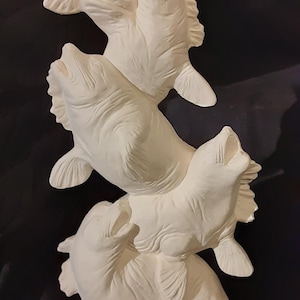 May include: A white ceramic sculpture of four fish stacked on top of each other. The fish are all facing upwards with their mouths open. The sculpture is a whimsical and decorative piece.