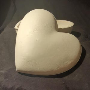 May include: A white ceramic heart-shaped box with a lid. The box is slightly open, revealing the inside.