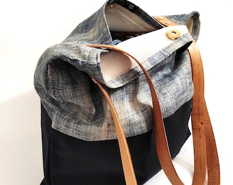 May include: A tote bag with a denim-like upper section and a solid black lower section. The bag features tan leather straps and a magnetic snap closure. The interior is visible, revealing a light-colored lining. The bag is designed for carrying items.