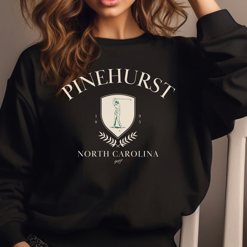 May include: Black sweatshirt with a white graphic design featuring the text "Pinehurst" in an arched design, a golfer silhouette, and the text "North Carolina golf".