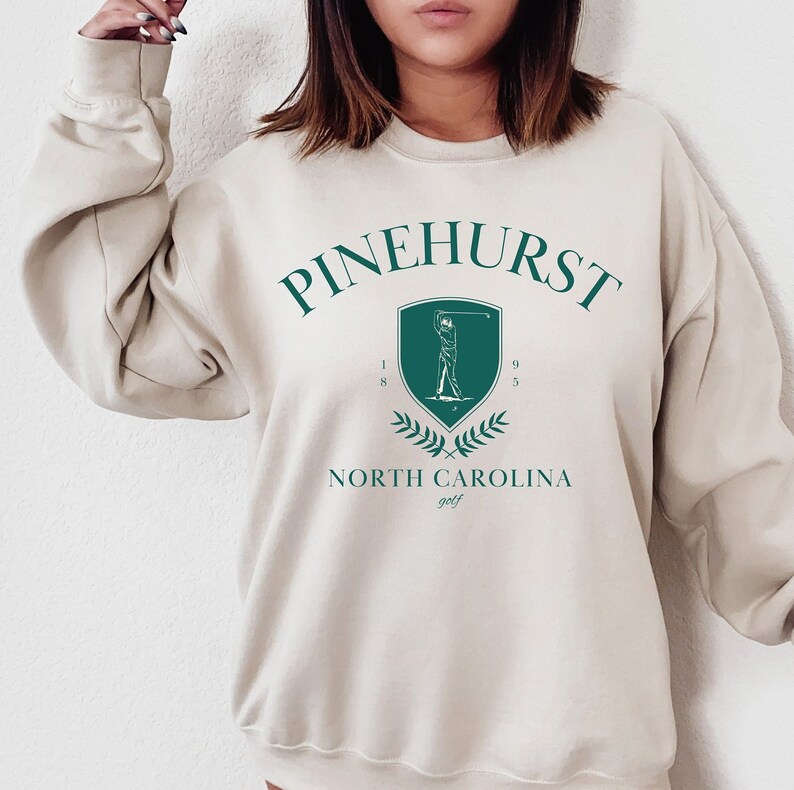 May include: A beige sweatshirt with a green graphic of a golfer and the text "Pinehurst 1895 North Carolina golf"