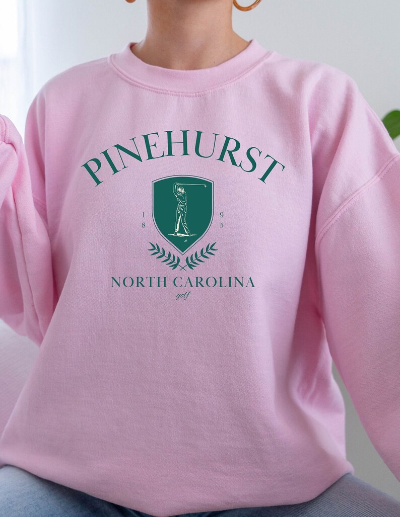 May include: Pink sweatshirt with a green graphic of a golfer and the text "Pinehurst North Carolina golf" with the numbers "1895" on the shield.