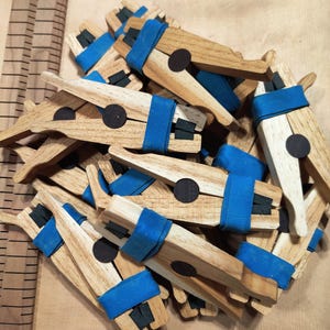 May include: A pile of wooden clamps with blue rubber bands and black circular pads. The clamps are used for woodworking projects.