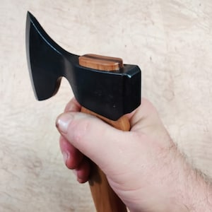 May include: A black axe with a wooden handle. The handle has a brown and black wood inlay at the top.