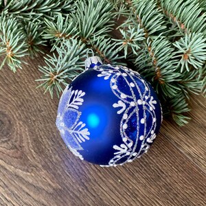 May include: A blue Christmas ornament with a white snowflake design. The ornament is sitting on a wooden surface.