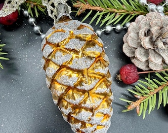May include: A gold and silver pinecone ornament with a textured surface. The ornament is surrounded by evergreen branches, red berries, and silver beads. The ornament is a festive decoration for the holiday season.