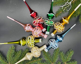 May include: Eight vintage glass Christmas tree toppers in various colors and designs. The toppers are shaped like a double bulb with a pointed top and feature white floral patterns.