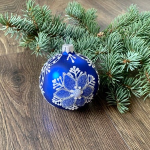May include: A blue Christmas ornament with a white snowflake design. The ornament is sitting on a wooden surface.