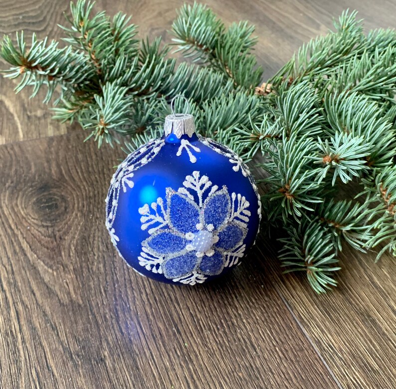 May include: A blue Christmas ornament with a white snowflake design. The ornament is sitting on a wooden surface.