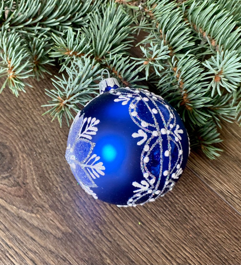 May include: A blue Christmas ornament with a white snowflake design. The ornament is sitting on a wooden surface.
