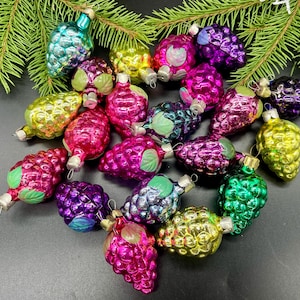 May include: A collection of vintage glass Christmas ornaments shaped like bunches of grapes. The ornaments are in various colors, including purple, green, pink, yellow, and blue.