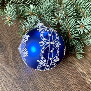 May include: A blue Christmas ornament with a white snowflake design. The ornament is made of glass and has a shiny finish.