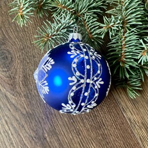 May include: A blue Christmas ornament with a white snowflake design. The ornament is decorated with silver glitter.