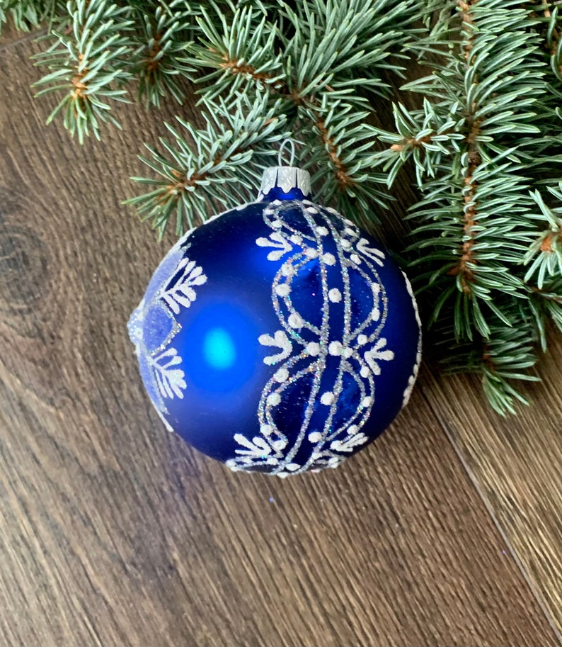 May include: A blue Christmas ornament with a white snowflake design. The ornament is decorated with silver glitter.