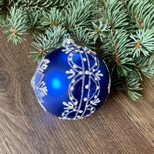 May include: A blue Christmas ornament with a white snowflake design. The ornament is made of glass and has a shiny finish.