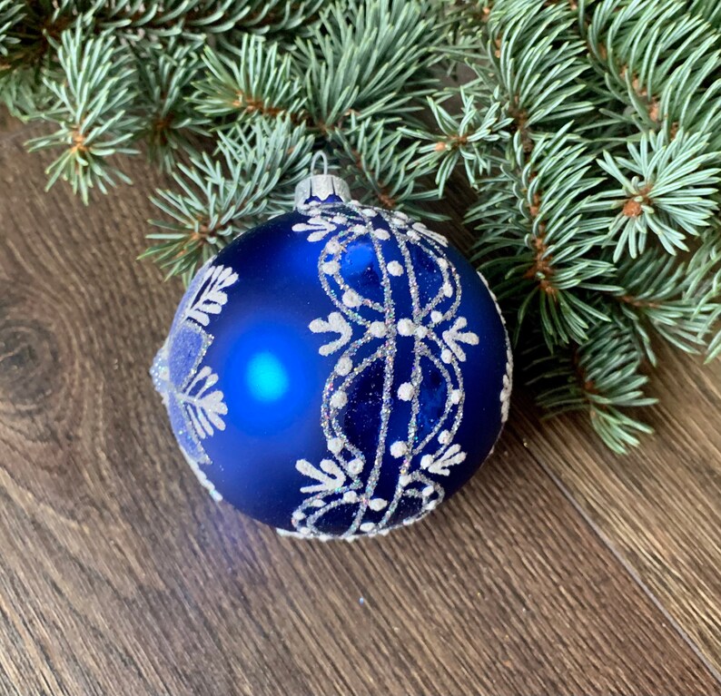 May include: A blue Christmas ornament with a white snowflake design. The ornament is made of glass and has a shiny finish.